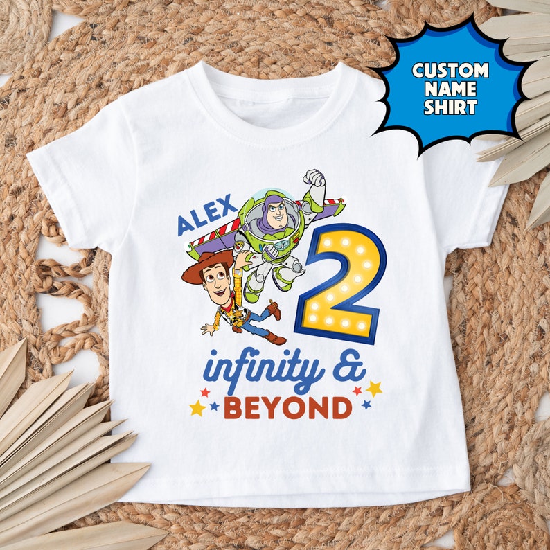 May include: White t-shirt with a custom name, "ALEX", and a graphic of Buzz Lightyear and Woody from Toy Story. The graphic includes the number "2" with lights around it and the text "infinity & BEYOND".