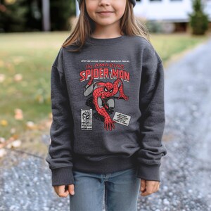 May include: A dark grey sweatshirt with a vintage comic book design featuring Spider-Man. The text on the shirt reads "The Amazing Spider-Man".