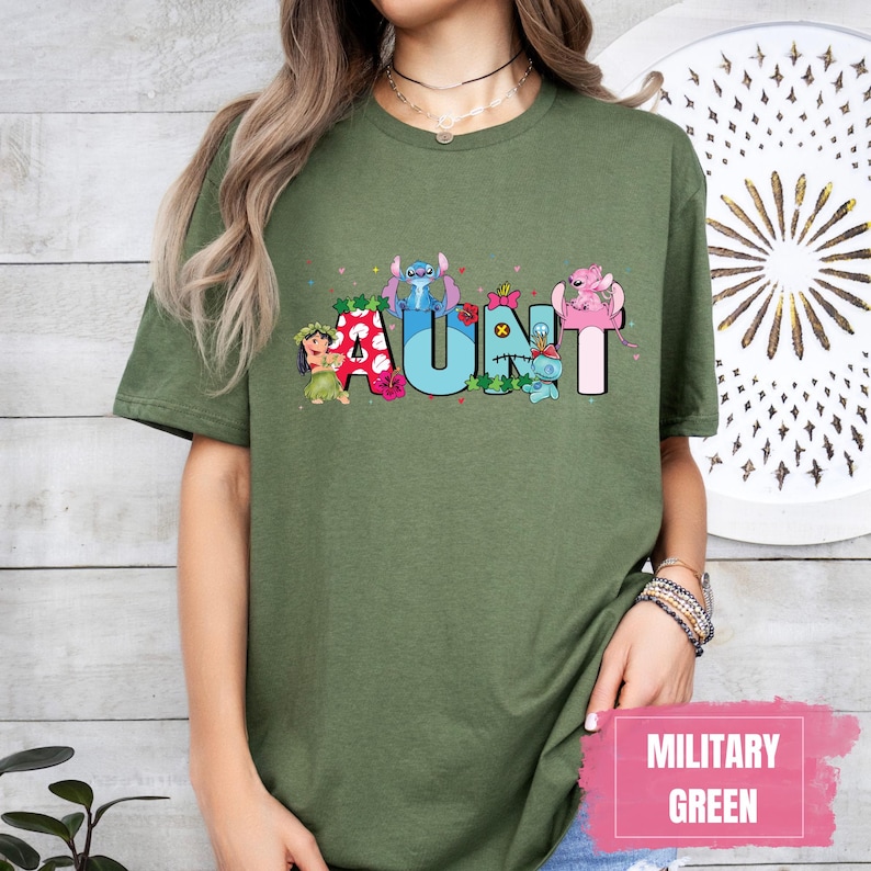 Puede incluir: Una camiseta verde con un gr&aacute;fico de personajes de Stitch que deletrean "AUNT" en letras de colores. La camiseta es de corte holgado y tiene cuello redondo.