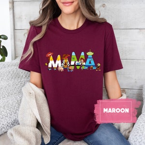 K&ouml;nnte beinhalten: Ein maroonfarbenes T-Shirt mit einem Aufdruck der Toy Story-Charaktere, die "MAMA" buchstabieren.