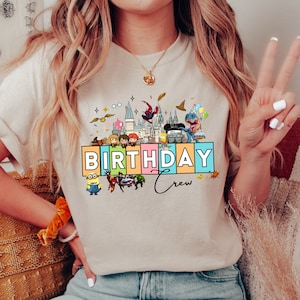 May include: Beige t-shirt with a colorful graphic that says "BIRTHDAY Crew". The graphic includes cartoon characters from various franchises, such as Harry Potter, Spider-Man, and Minions. The shirt has a crew neck and short sleeves.