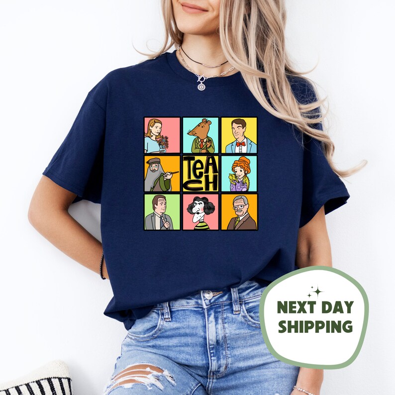May include: Navy blue t-shirt featuring a colorful grid of cartoon characters and the word "TEACH". The design includes images of a woman with flowers, a rodent in a suit, and other figures. A fun and educational theme.
