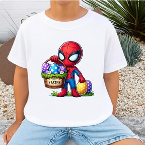 Puede incluir: Camiseta blanca con un personaje de dibujos animados de Spider-Man sosteniendo una cesta de Pascua. La cesta tiene el texto "Happy Easter". Los huevos est&aacute;n decorados con varios patrones y colores. El personaje lleva un traje rojo y azul.