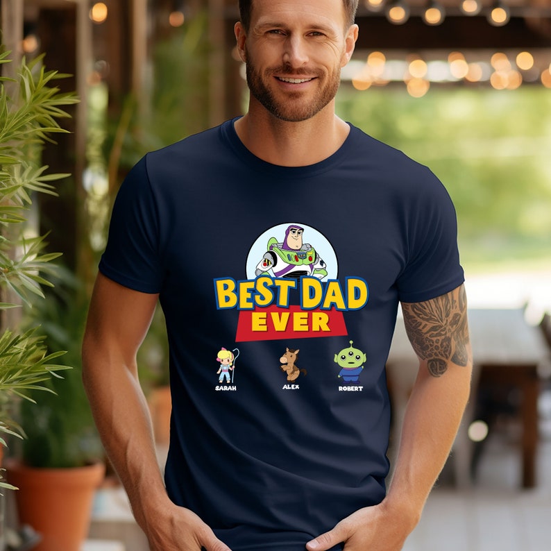 May include: Navy blue t-shirt featuring a graphic of Buzz Lightyear and the text "BEST DAD EVER". Below the text are cartoon characters and names. A man is wearing the shirt.