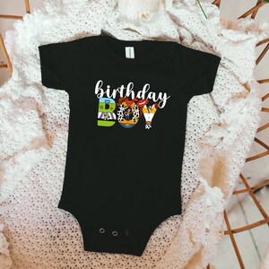 K&ouml;nnte beinhalten: Schwarzer Strampler mit einer wei&szlig;en Grafik des Wortes "Geburtstag" und des Wortes "BOY", das aus Bildern aus dem Toy Story-Film-Franchise besteht.