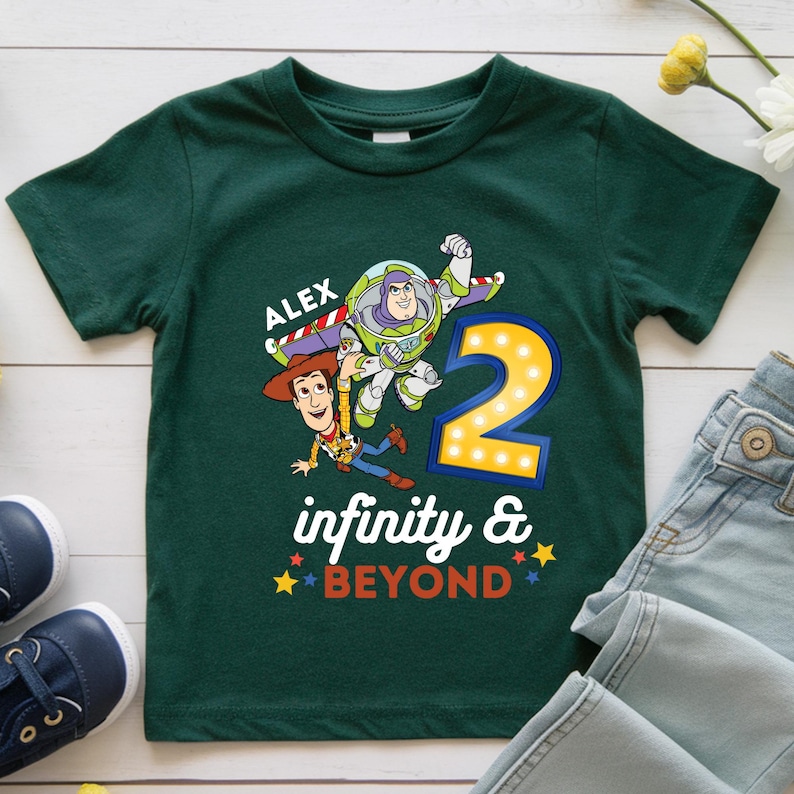 K&ouml;nnte beinhalten: Ein dunkelgr&uuml;nes T-Shirt mit einer Grafik von Buzz Lightyear und Woody aus Toy Story. Die Zahl "2" wird mit den Worten "infinity & BEYOND" angezeigt. Der Name "ALEX" ist &uuml;ber den Figuren aufgedruckt.