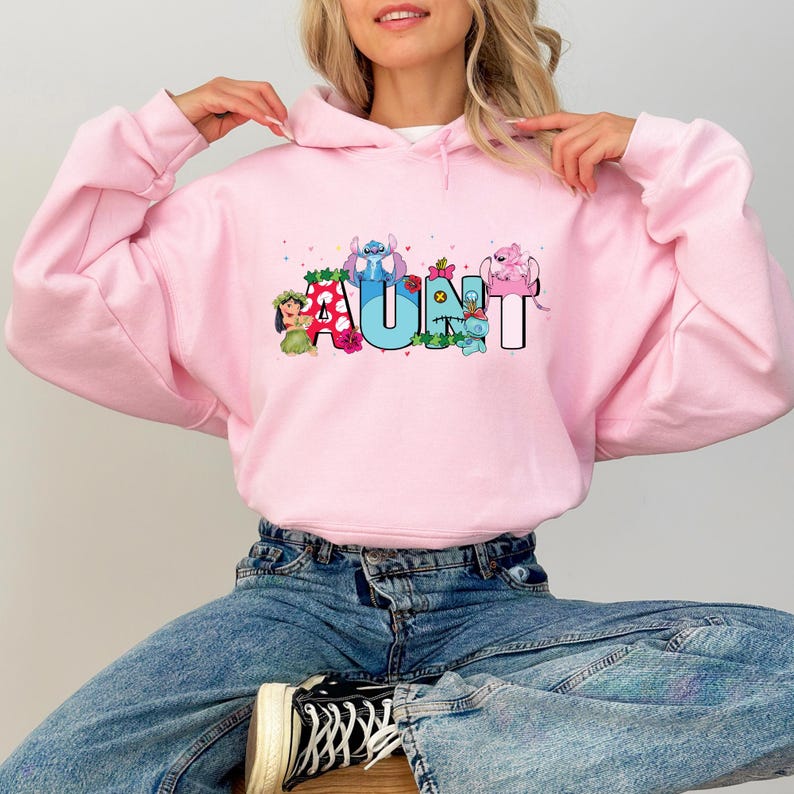 May include: Pink hooded sweatshirt with a graphic print of the word "AUNT" with cartoon characters. The characters are Stitch, Lilo, and other Disney characters.