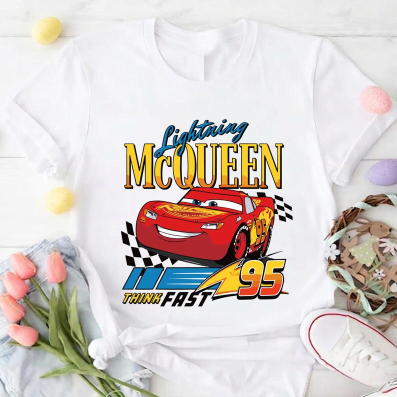 May include: White t-shirt featuring a graphic of Lightning McQueen from the movie Cars. The design includes the text "Lightning McQueen" in yellow and blue, the number "95", and the phrase "Think Fast".
