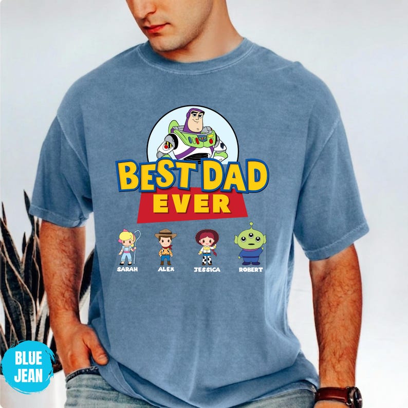 May include: Blue t-shirt with the text "BEST DAD EVER" in yellow and red, featuring a cartoon image of Buzz Lightyear and four cartoon characters. The names "SARAH", "ALEX", "JESSICA", and "ROBERT" are printed below the characters.