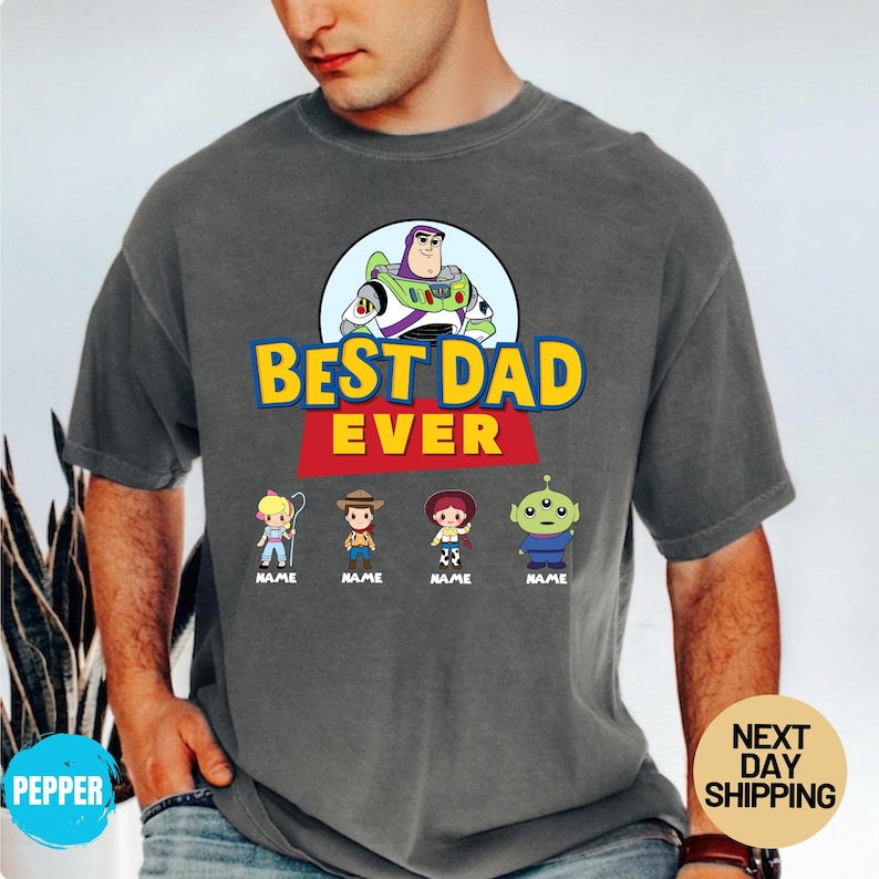 May include: Dark grey t-shirt with the text "BEST DAD EVER" in yellow and red, and a Buzz Lightyear graphic. Below are cartoon characters with the word "NAME" under each. The t-shirt is a casual style.