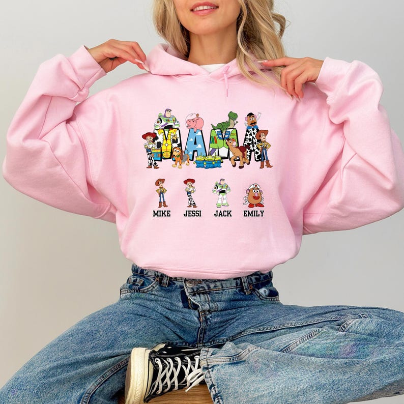 Może przedstawiać: R&oacute;żowa bluza z nadrukiem postaci z Toy Story, kt&oacute;re tworzą napis "MAMA" z nazwami "Mike, Jessi, Jack, Emily" pod spodem.