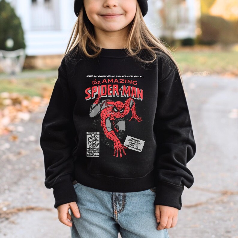 May include: A black sweatshirt with a vintage comic book design featuring Spider-Man. The text on the shirt reads "The Amazing Spider-Man".