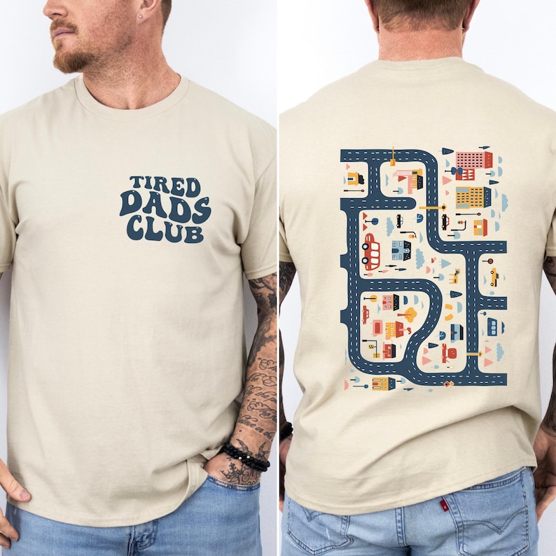 Pu&ograve; includere: T-shirt beige con la scritta "TIRED DADS CLUB" in blu navy sul davanti. Il retro della maglietta presenta un design colorato a mappa stradale con edifici, auto e alberi. Una maglietta casual e confortevole.