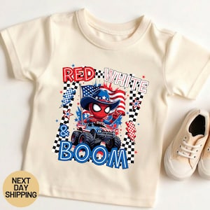 May include: Cream-colored t-shirt featuring a graphic of Spider-Man in a cowboy hat driving a monster truck with a flag. The text reads "RED, WHITE & BOOM". The shirt has a round neck and short sleeves.