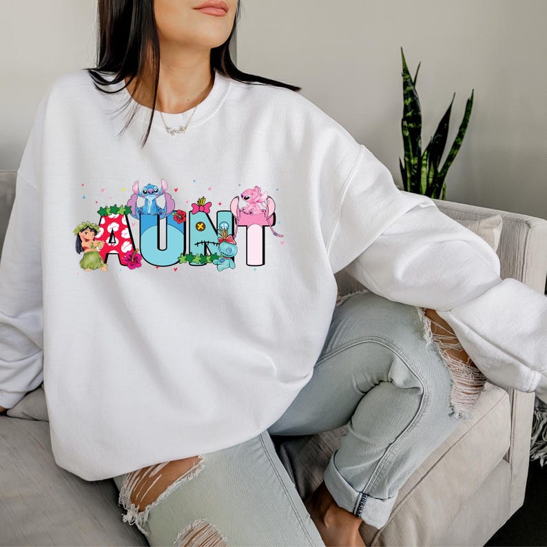 May include: White sweatshirt with a graphic design of the word "AUNT" spelled out with cartoon characters. The characters are from the Disney movie Lilo & Stitch.