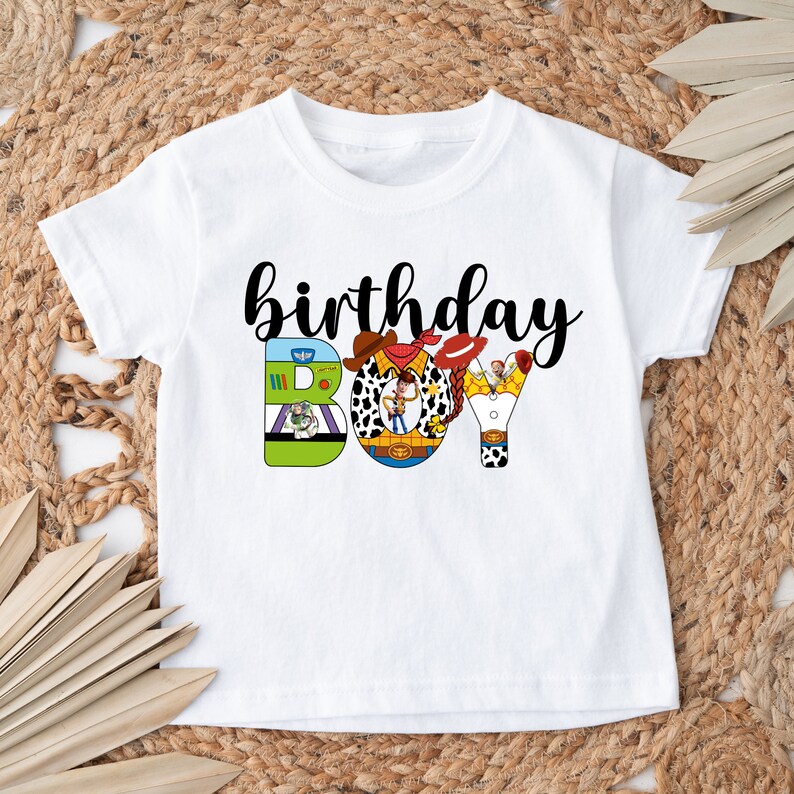 K&ouml;nnte beinhalten: Wei&szlig;es T-Shirt mit einer schwarz-wei&szlig;en Grafik von Toy Story-Charakteren, die "birthday boy" buchstabieren.