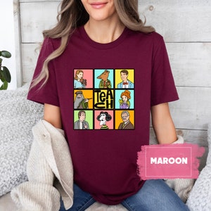 May include: Maroon t-shirt featuring a grid of cartoon characters with the word "TEACH" in the center. The characters are set against colorful backgrounds. The shirt is a solid maroon color.