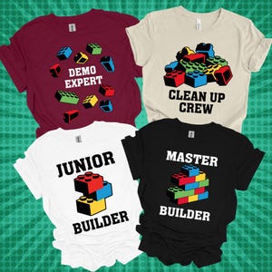 May include: Four t-shirts in burgundy, cream, white, and black. Each shirt features a colorful graphic of toy building blocks and text: "DEMO EXPERT", "CLEAN UP CREW", "JUNIOR BUILDER", and "MASTER BUILDER".