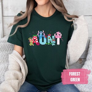 Puede incluir: Una camiseta verde bosque con un gr&aacute;fico de Stitch y otros personajes de Disney que deletrean "AUNT".