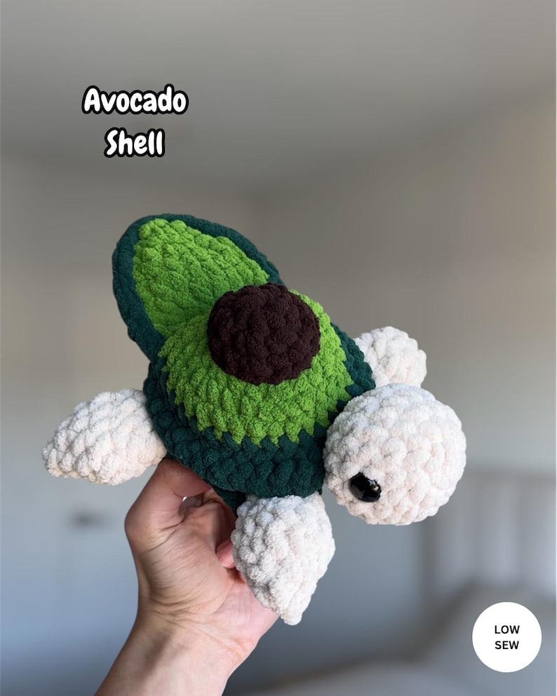 May include: A crochet plush toy shaped like a turtle with an avocado shell pattern. The shell features dark green, light green, and a brown center. The head and flippers are made of white yarn. Text on the image reads Avocado Shell and LOW SEW.