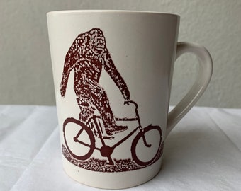 Sasquatch Big Foot Riding a Bike White Ceramic Porcelain Coffee Cup 12 & half oz.