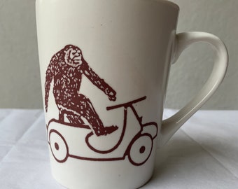 Sasquatch Big Foot Riding on a Scooter White Ceramic Porcelain Coffee Cup 12 & half oz.