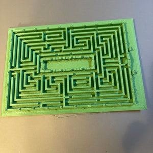 May include: A green 3D printed maze with a rectangular shape. The maze has a central open area and a complex network of paths.