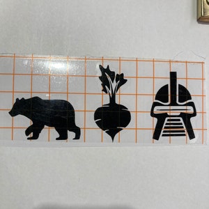 May include: Black silhouette decals of a bear, a beet, and a helmet. The decals are on a white grid background.