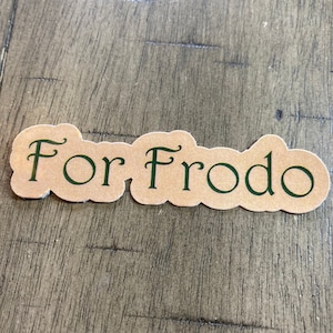 May include: A brown paper sticker with the text "For Frodo" written in green cursive lettering.