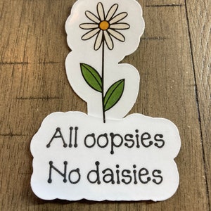May include: White daisy sticker with green leaves and the text "All oopsies No daisies" in black.