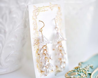 May include: A pair of dangle earrings with clear crystal beads and gold accents. The earrings are displayed on a white card with a gold border.