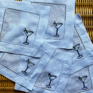 Peut inclure: Ensemble de six serviettes de cocktail en lin bleu avec des verres &agrave; martini et des olives brod&eacute;s. Les serviettes ont une bordure blanche et sont parfaites pour recevoir.