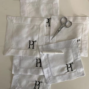 Peut inclure: Une pile de serviettes en lin blanc avec des initiales "P" brod&eacute;es en noir. Les serviettes sont pli&eacute;es en forme de carr&eacute; et ont une bordure d&eacute;corative.