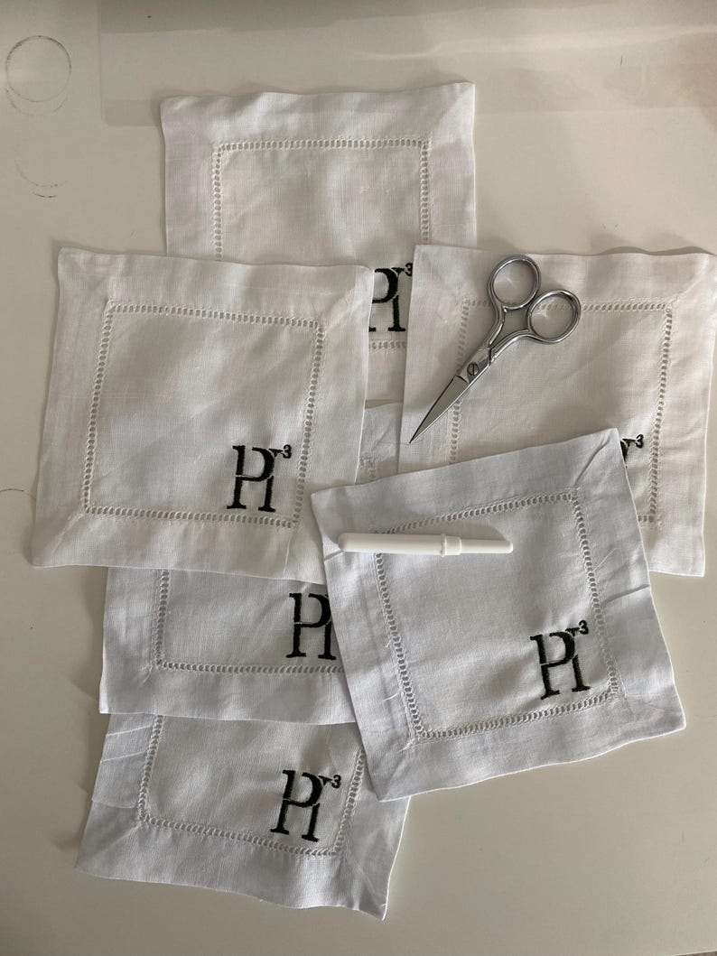 Peut inclure: Une pile de serviettes en lin blanc avec des initiales "P" brod&eacute;es en noir. Les serviettes sont pli&eacute;es en forme de carr&eacute; et ont une bordure d&eacute;corative.