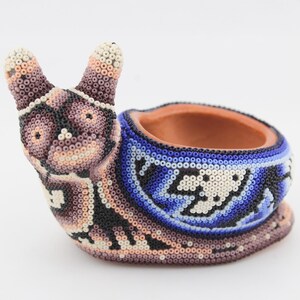 May include: A handcrafted snail-shaped planter, adorned with intricate beadwork. The snail's body features a mix of colors, including brown, black, white, and blue. The planter's opening is a terracotta color, providing a striking contrast to the beaded exterior.
