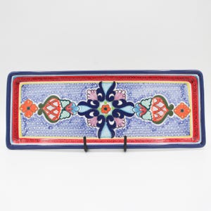 May include: A rectangular ceramic serving tray featuring a central blue and white dotted pattern with a symmetrical floral motif in shades of dark blue, light blue, pink, and orange. The tray has a thick dark blue border and a red inner trim.