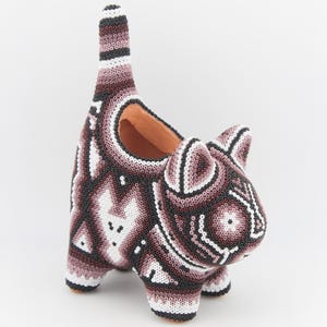 May include: A cat-shaped planter covered in intricate beadwork featuring a geometric pattern in shades of brown, black, and white. The hollow interior reveals a terracotta-colored clay base, and the upright tail forms a tall, slender structure.