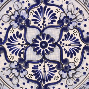 Pode incluir: Um prato de cer&acirc;mica branco com um design floral azul e branco. O design apresenta v&oacute;rtices e flores intrincados.