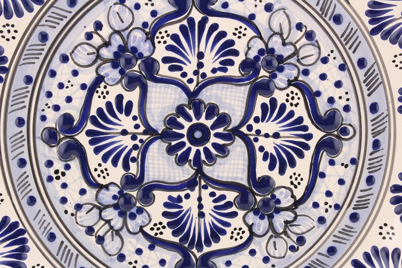 Pode incluir: Um prato de cer&acirc;mica branco com um design floral azul e branco. O design apresenta v&oacute;rtices e flores intrincados.