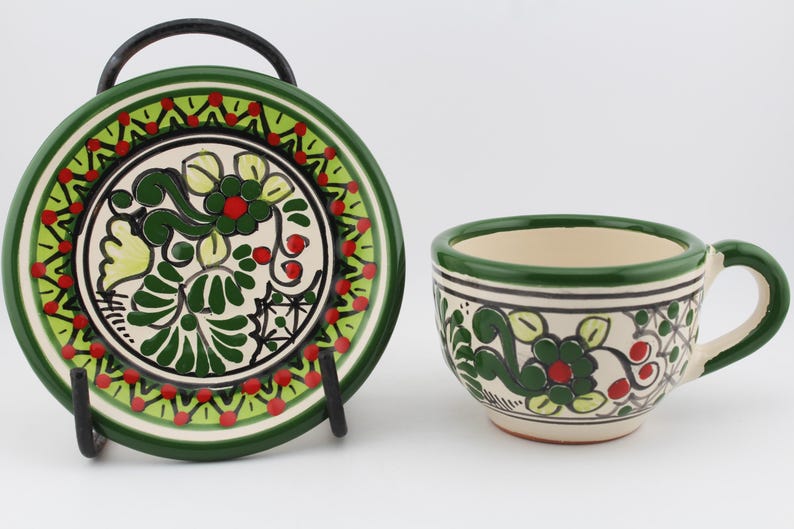 May include: A green and white ceramic teacup and saucer set with a floral design. The cup has a handle and the saucer has a rim.