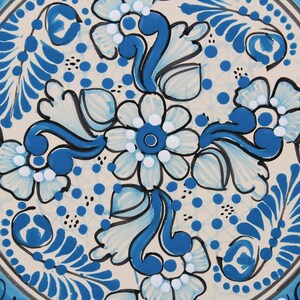 Pode incluir: Um prato de cer&acirc;mica branco com um design floral azul e branco. O prato apresenta um padr&atilde;o repetitivo de flores e folhas, com um motivo central de uma flor maior.