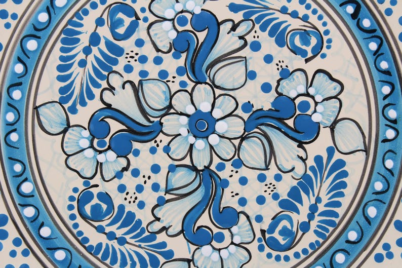 Pode incluir: Um prato de cer&acirc;mica branco com um design floral azul e branco. O prato apresenta um padr&atilde;o repetitivo de flores e folhas, com um motivo central de uma flor maior.