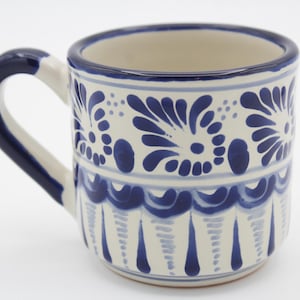 May include: A white ceramic mug with a blue and white floral design. The mug has a handle and is decorated with a traditional Mexican Talavera pattern.