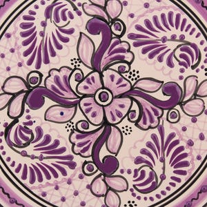 Pode incluir: Um prato de cer&acirc;mica branco com um design floral roxo. O design apresenta uma flor central de quatro p&eacute;talos e folhas em espiral. O prato &eacute; decorado com uma borda de pequenos pontos roxos.