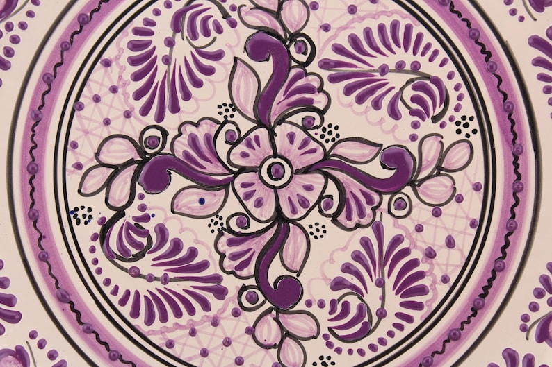 Pode incluir: Um prato de cer&acirc;mica branco com um design floral roxo. O design apresenta uma flor central de quatro p&eacute;talos e folhas em espiral. O prato &eacute; decorado com uma borda de pequenos pontos roxos.