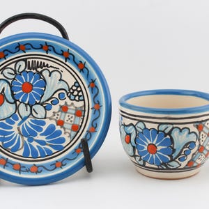 May include: A blue and white ceramic teacup and saucer set with a floral design. The cup has a handle and the saucer has a black metal stand.