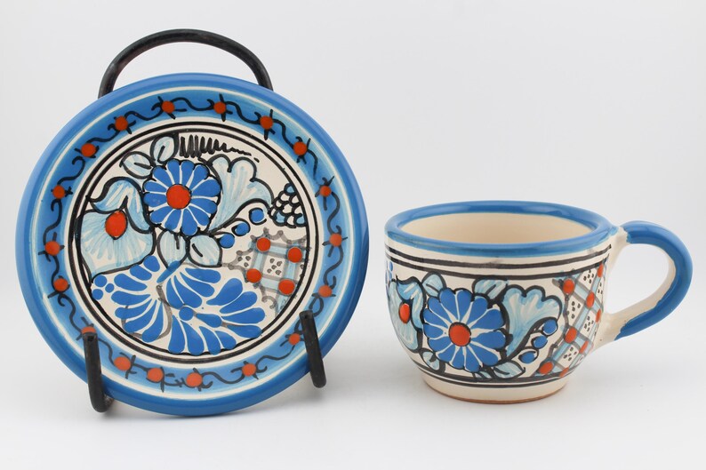 May include: A blue and white ceramic teacup and saucer set with a floral design. The cup has a handle and the saucer has a black metal stand.