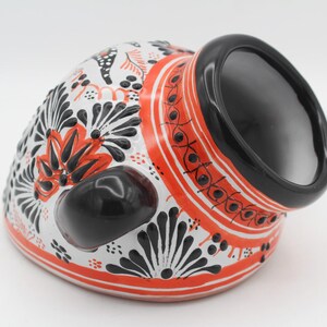 May include: A ceramic vessel with a black interior and exterior accents. The exterior features a white base with black and red floral patterns. The rim and a side accent are black, and the vessel has a rounded shape.