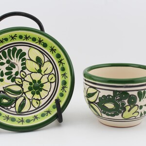 May include: A green and white ceramic teacup and saucer set with a floral design. The cup has a handle and the saucer has a stand.