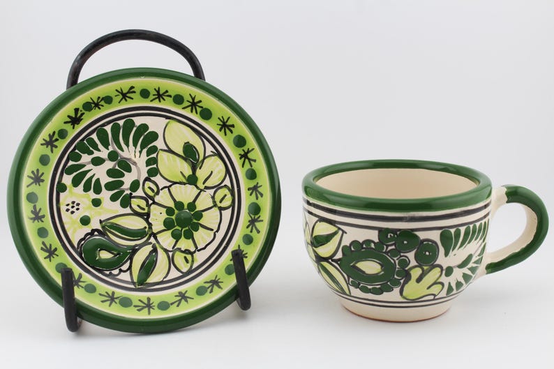 May include: A green and white ceramic teacup and saucer set with a floral design. The cup has a handle and the saucer has a stand.